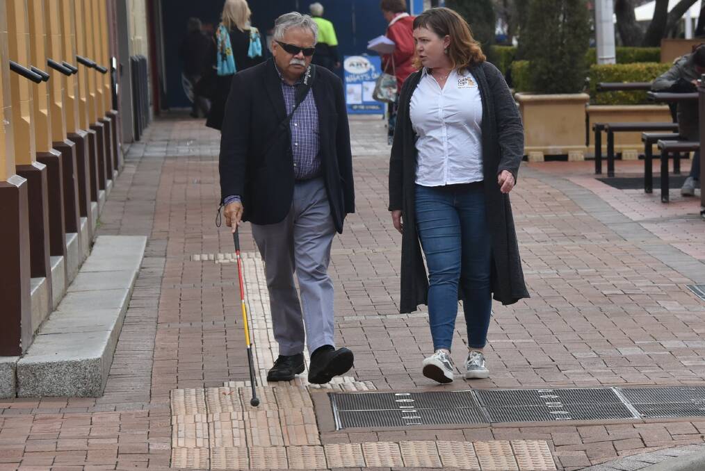 Steve Widders "feels" the Tactile Ground Surface Indicator tiles on the footpath as he walks along with Tamson Mayo.